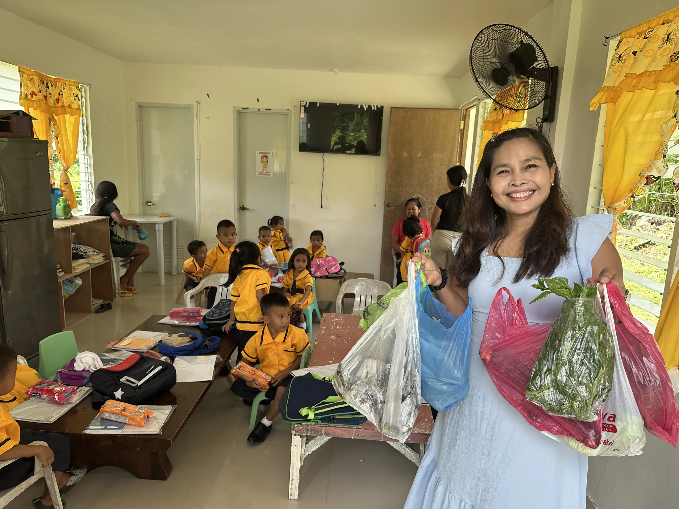 A woman holding bags of supplies in a classroom with children